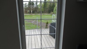 Uitzicht door een raam, met een houten terras en een sportveld op de achtergrond.