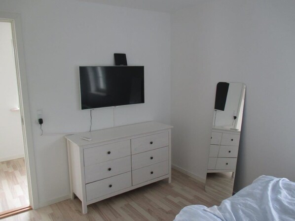 Un dormitorio con un aparador blanco, un televisor de pantalla plana montado encima y un espejo sobre el aparador.