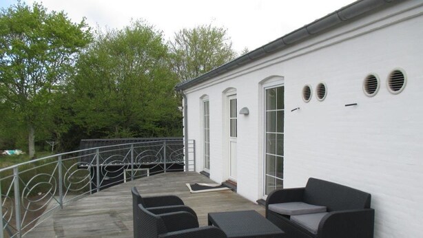 Een overdekt buitengebied met een wit gebouw, een metalen hekwerk en tuinmeubilair.
