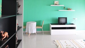 A modern living room with a green wall, white shelves, a small round table, and a TV on a white stand. - Greenville Serviced Apartment (Khlong Luang)