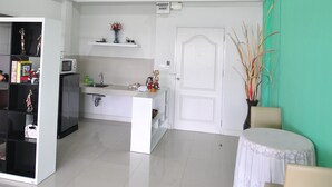 A spacious room with a kitchen area, a dining table with chairs, and a door leading to another room. - Greenville Serviced Apartment (Khlong Luang)