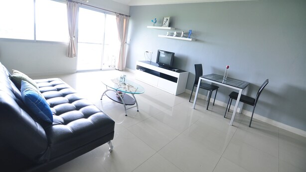 A modern living room with a sofa, a glass coffee table, a TV, and a dining table with chairs. - Greenville Serviced Apartment (Khlong Luang)
