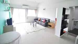 A spacious living room with a sofa, coffee table, and a view of the outside. - Greenville Serviced Apartment (Khlong Luang)