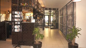 A lobby with a reception desk, a wall-mounted wine rack, and two potted plants. - Escale Hotel (Brussels)