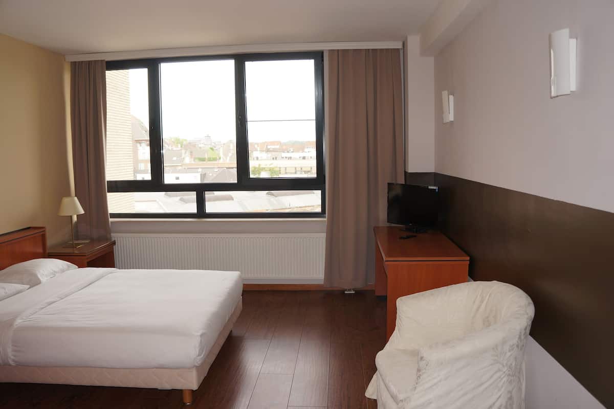 Una habitación de hotel con cama, sillón, televisión, ventana y radiador.