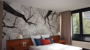 A bedroom with a bed, two nightstands, a large window, and a wall mural. - Escale Hotel (Brussels)