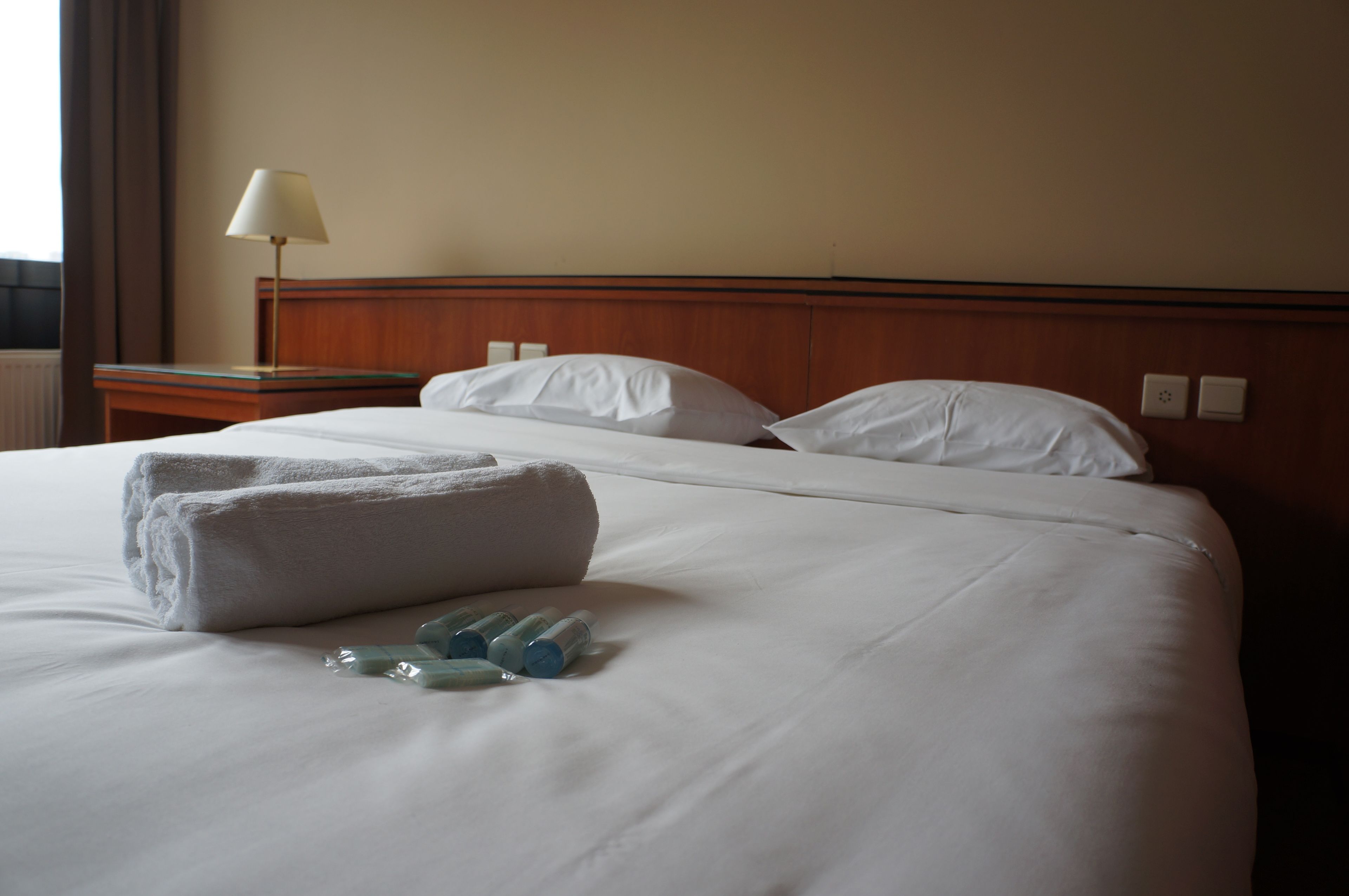 Ein Hotelzimmer mit einem ordentlich bezogenen Bett, einer Nachttischlampe und einem Nachttisch.