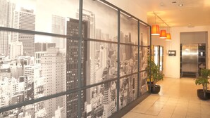 A modern hotel lobby with a cityscape mural, potted plants, and a visible elevator. - Escale Hotel (Brussels)