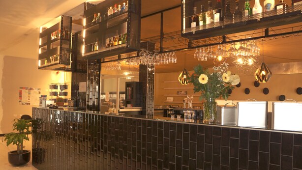 A bar area with shelves of bottles, glasses, and a potted plant. - Escale Hotel (Brussels)