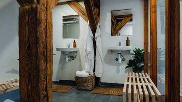 A bathroom with wooden beams, two sinks, a mirror, a plant, and a basket with towels.