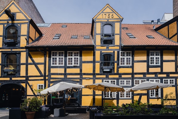 A traditional half-timbered building with a number '1756' on the facade, outdoor seating with umbrellas, and a small shop entrance.