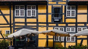 Ein traditionelles Fachwerkhäuschen mit der gut sichtbaren Jahreszahl '1756' an der Fassade, Außenplätzen mit Sonnenschirmen und einem Kopfsteinpflasterhof.