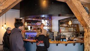 Eine Bar mit Holzbalken, einer Theke mit einem Schild mit der Aufschrift 'Café' und Regalen voller Flaschen und Gläser.