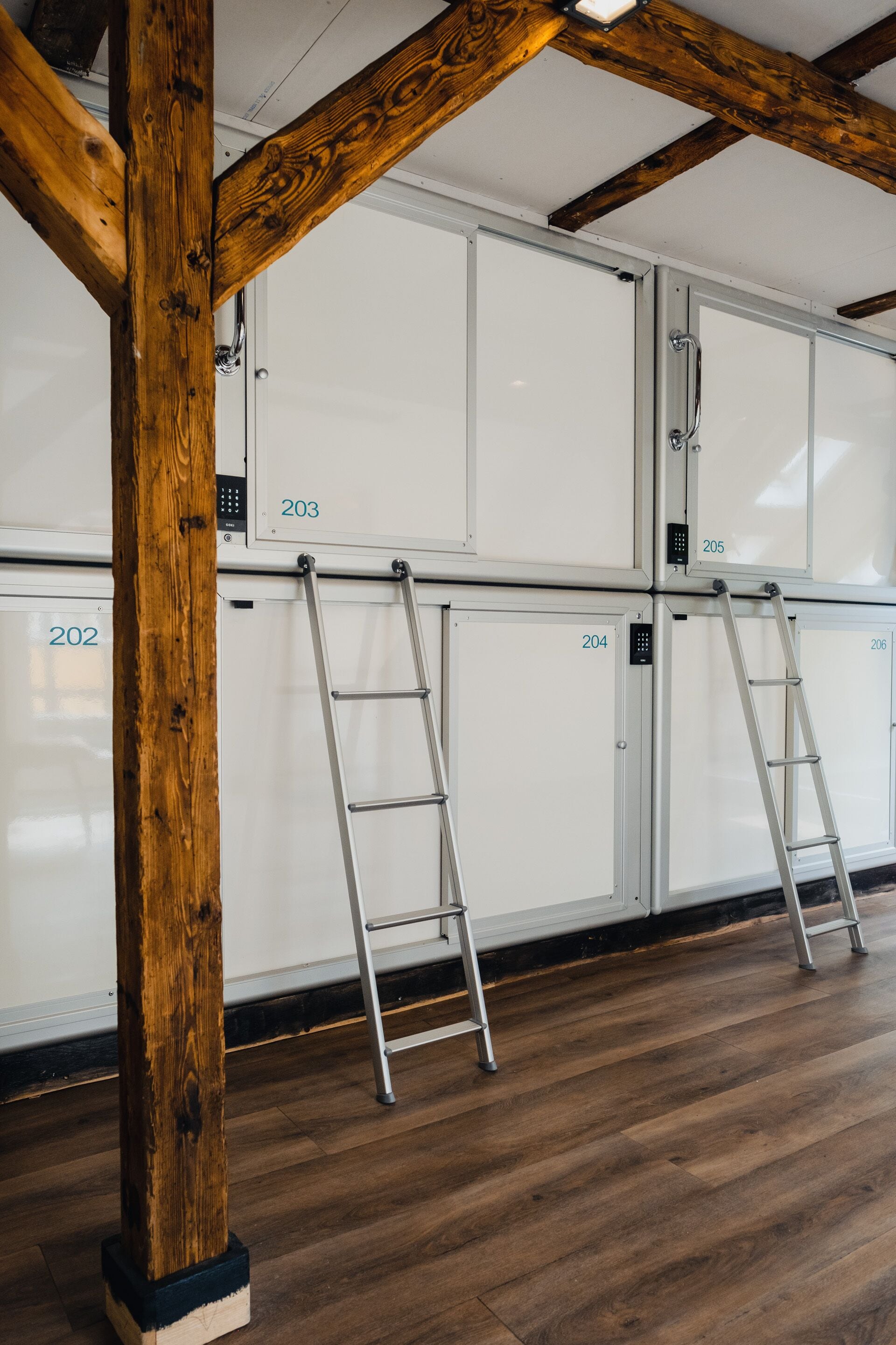 Een kamer met houten balken, witte kasten genummerd 202, 203, 204, 205 en 206, en twee metalen ladders die tegen de kasten leunen.