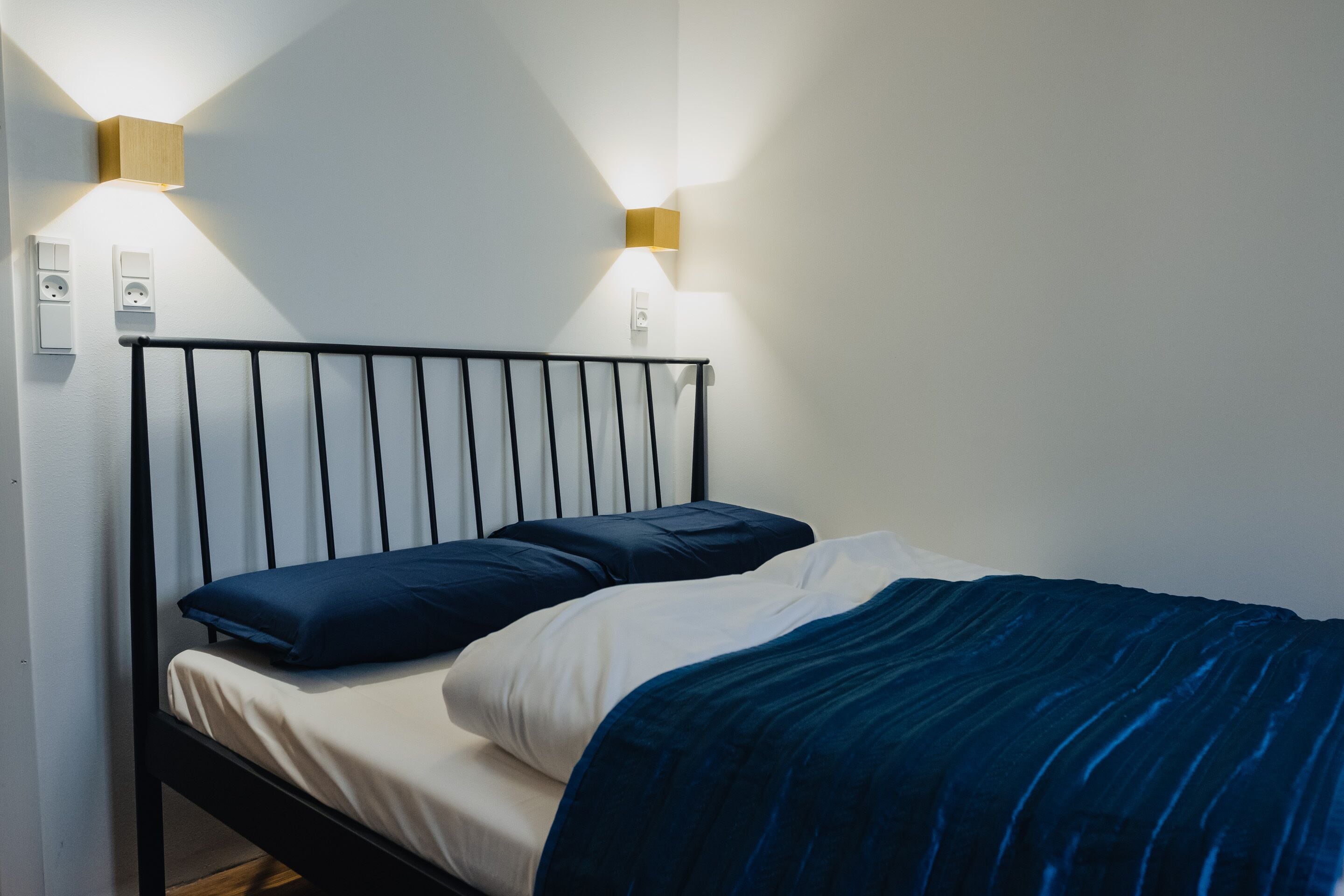 A bed with a black metal frame, two pillows, and a blue blanket.