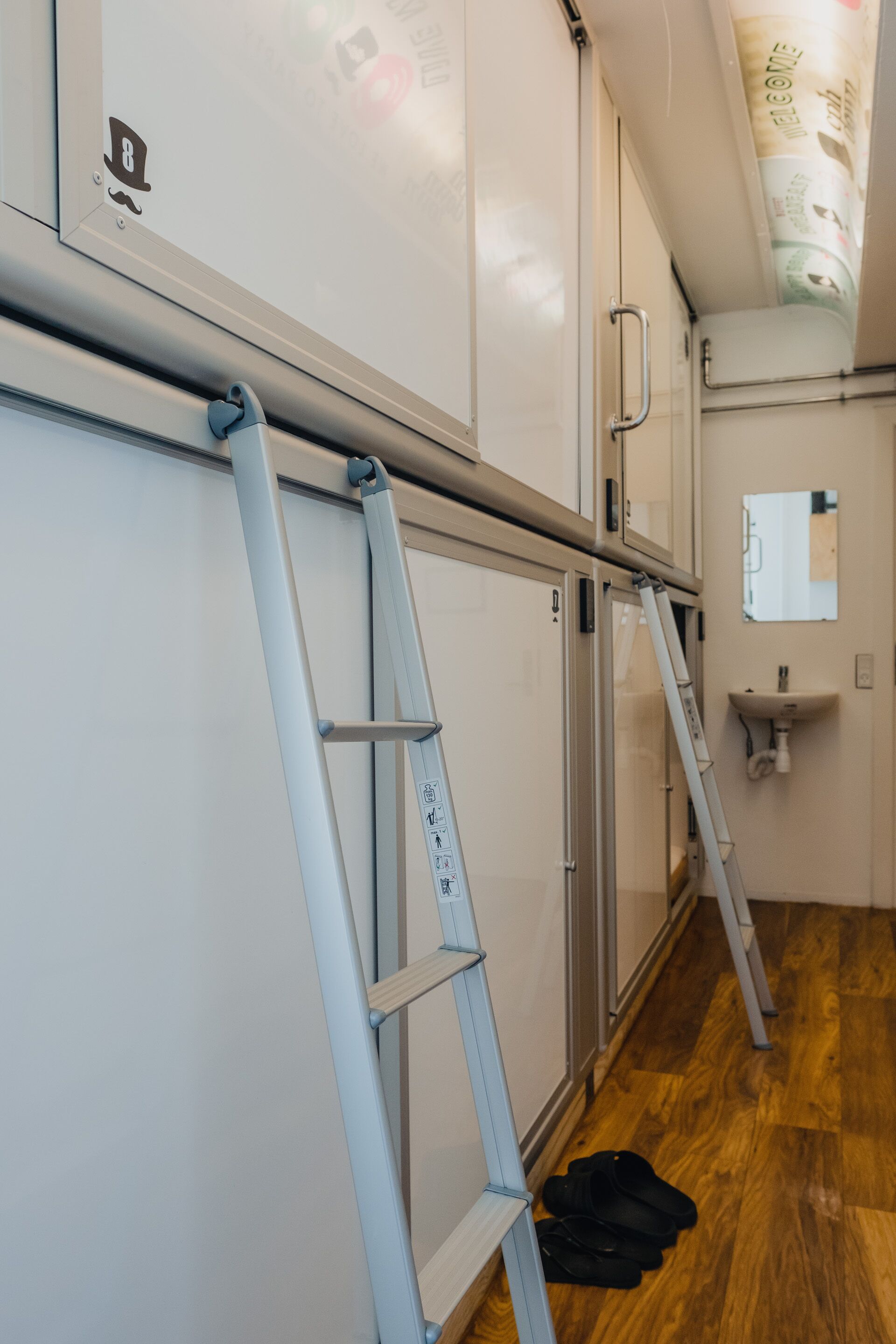 Una habitación con piso de madera, pared blanca con una puerta y techo blanco con lámpara.