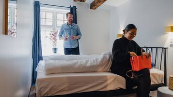 A modern hotel room with a bed, a window with curtains, a bedside table, and a lamp.