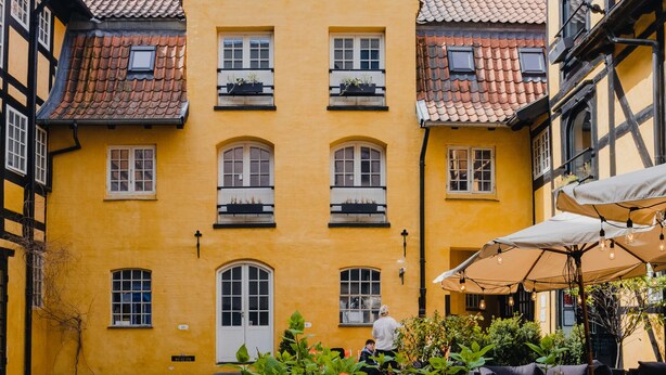 Ein Innenhof mit einem gelben Gebäude, Außenplätzen und einem Pflasterweg.