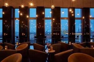 Ein modernes Restaurant mit hohen Decken, großen Fenstern und hängenden Leuchten.