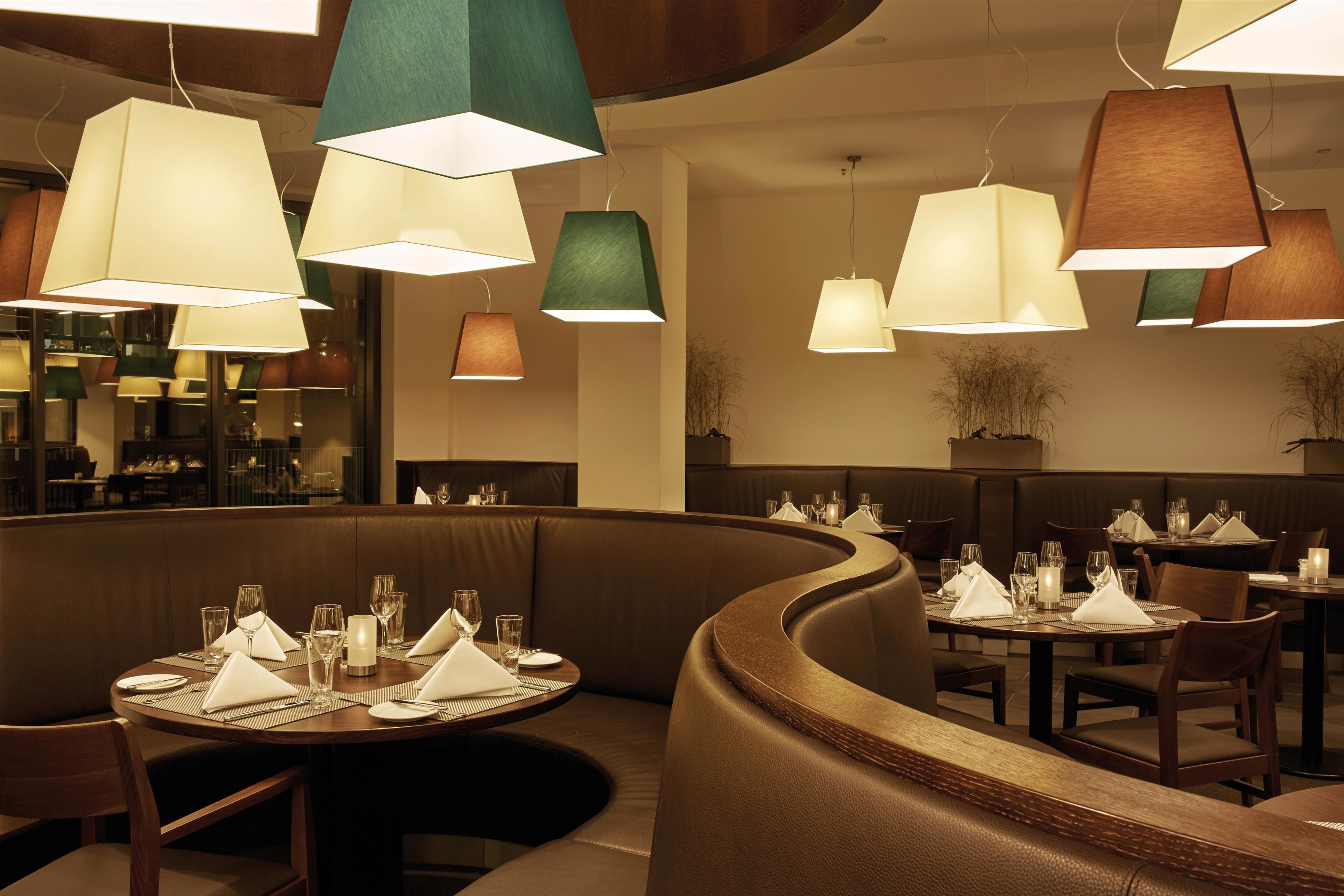 A restaurant with round tables set for dining, featuring a variety of pendant lights.