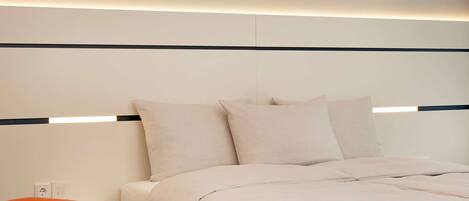 A modern hotel room with a neatly made bed, a small orange chair, and a wall-mounted light fixture.