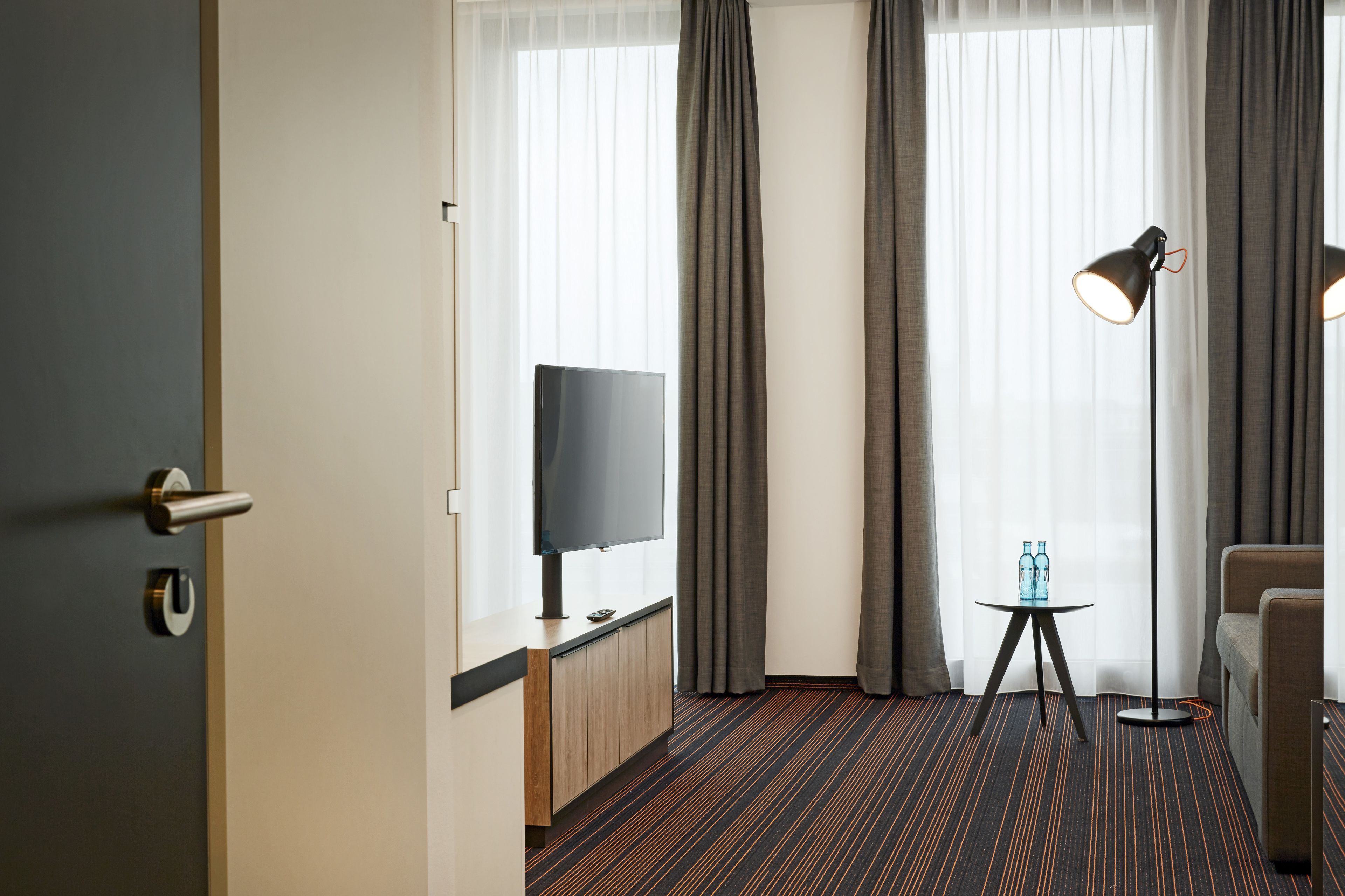 Une chambre d’hôtel avec une télévision, une petite table avec des bouteilles, une lampe et un canapé.