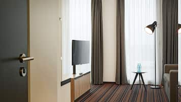 A hotel room with a TV, a small table with bottles, a lamp, and a sofa.