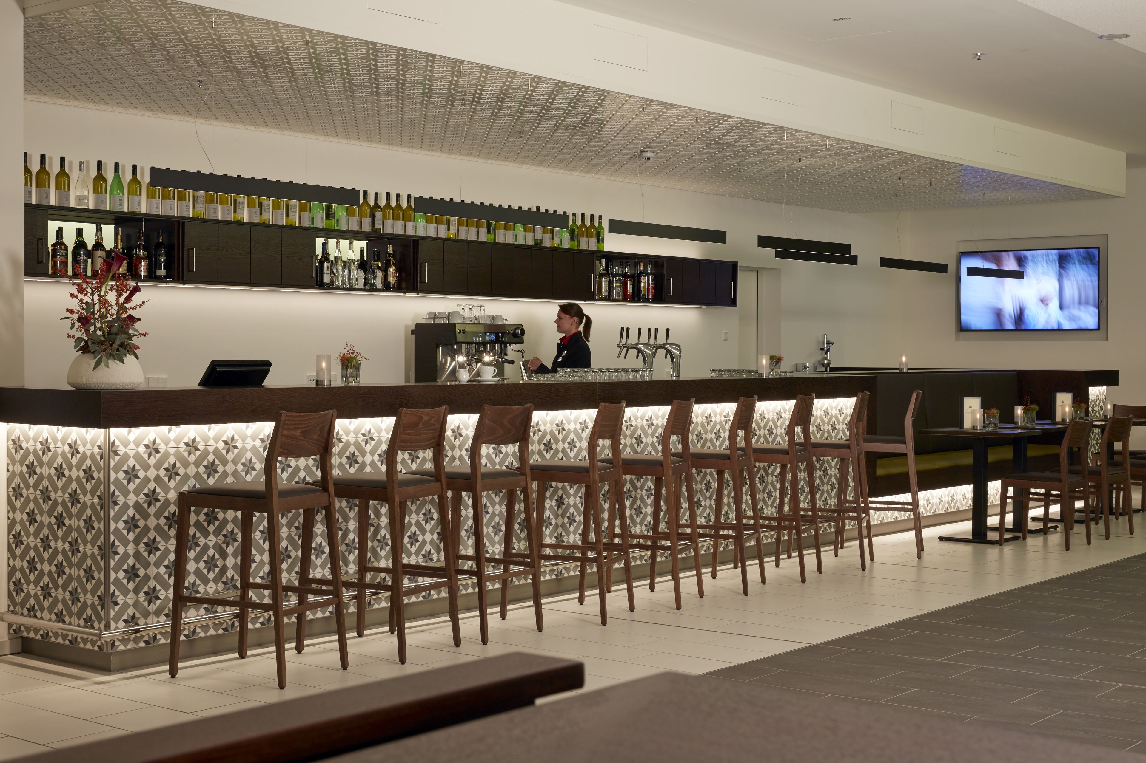 A bar area with a long counter, multiple bar stools, and a television mounted on the wall.