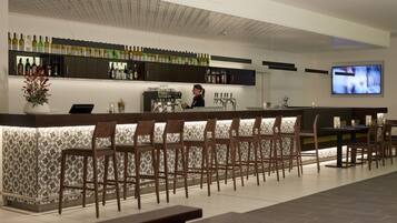 A bar area with a long counter, multiple bar stools, and a television mounted on the wall.