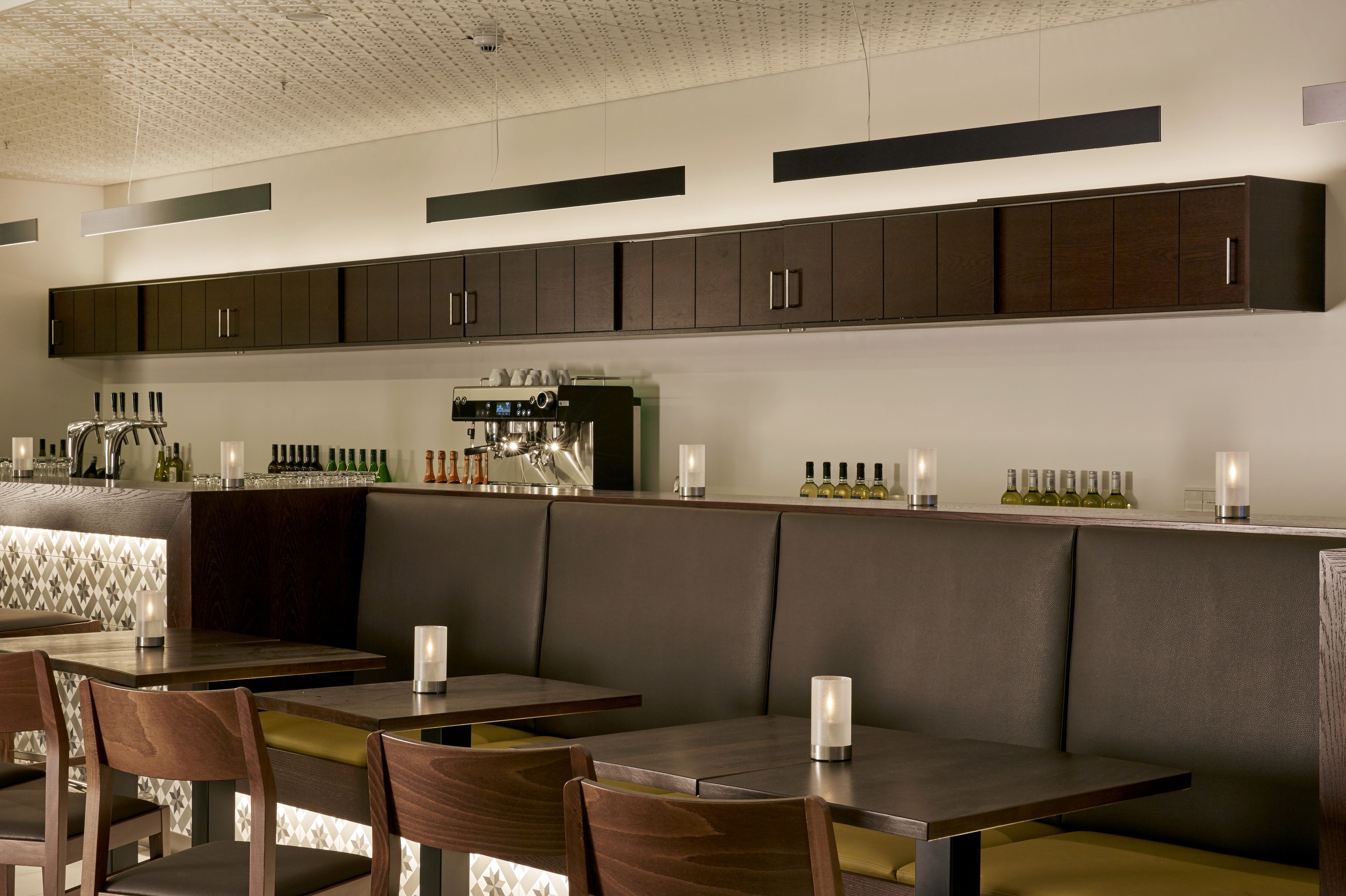 Un restaurante moderno con cabinas de madera oscura, una zona de bar con una máquina de café y botellas ordenadas en la barra.