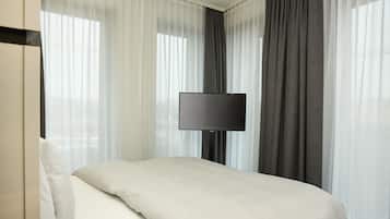 Una habitación de hotel con cama, televisión de pantalla plana, cortinas traslúcidas y una cortina oscura.