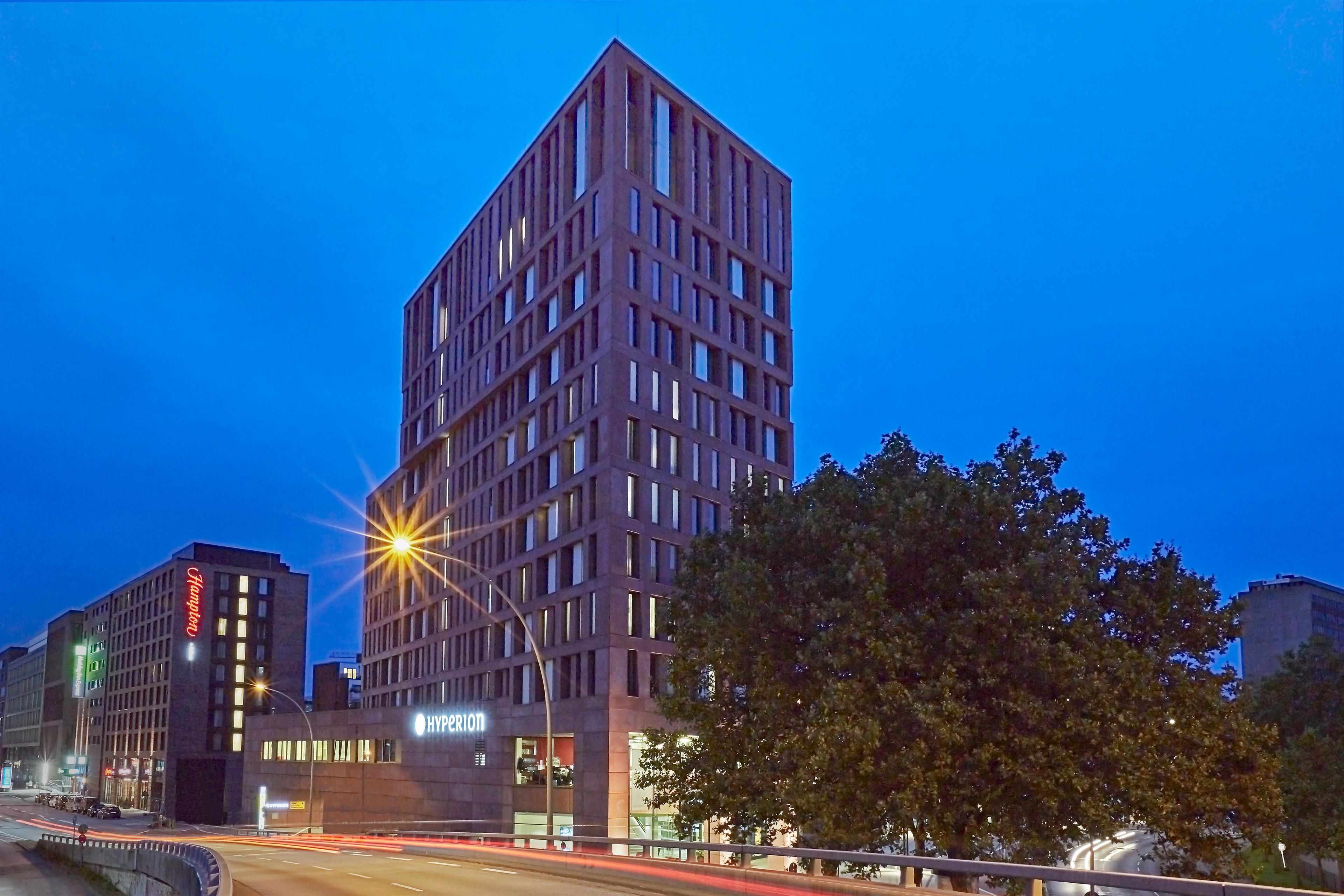 A modern hotel with a grid-like facade, illuminated windows, and a visible 'HyPerion' sign.