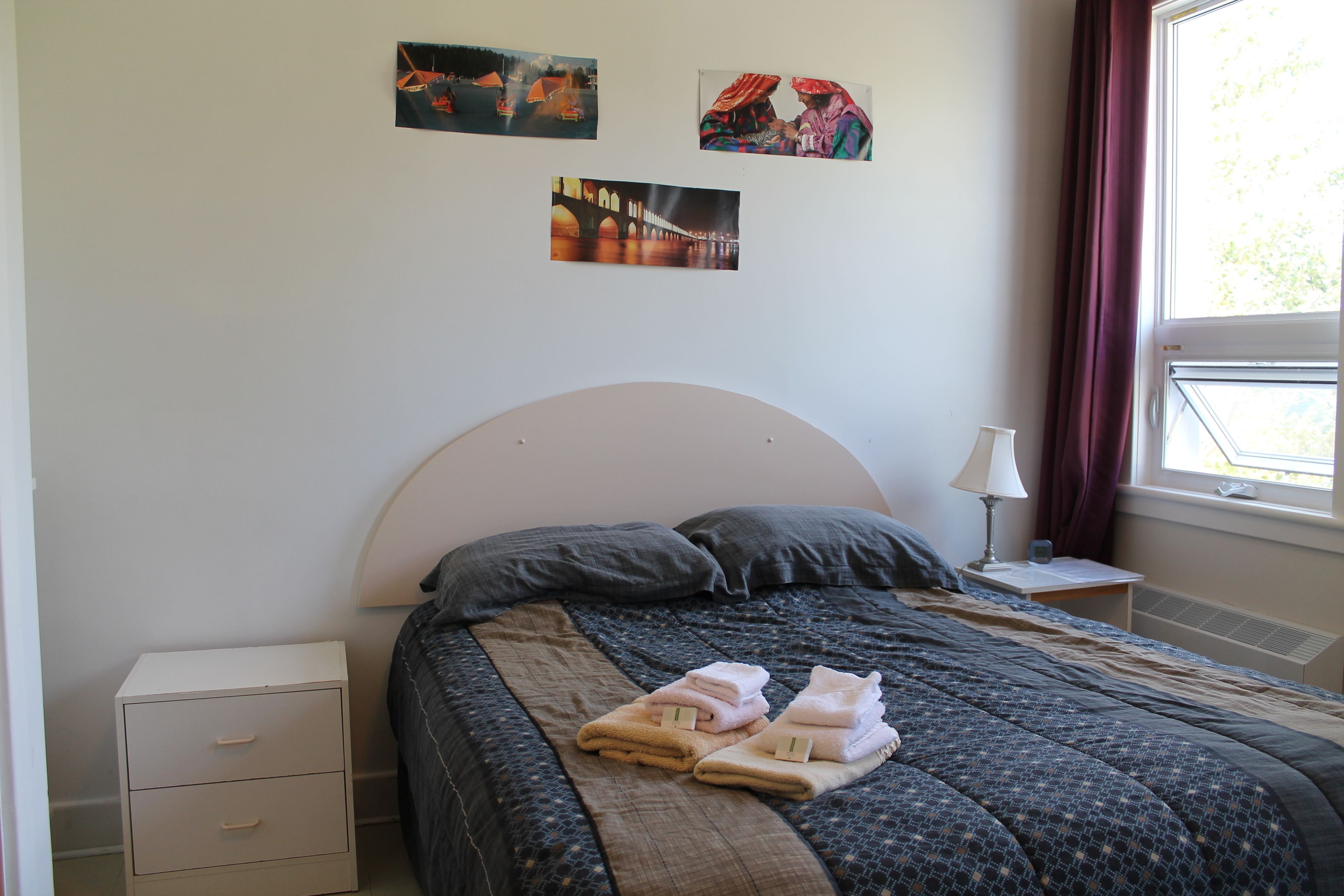 A neatly made bed with a headboard, a bedside table with a lamp, and a nightstand with a drawer.