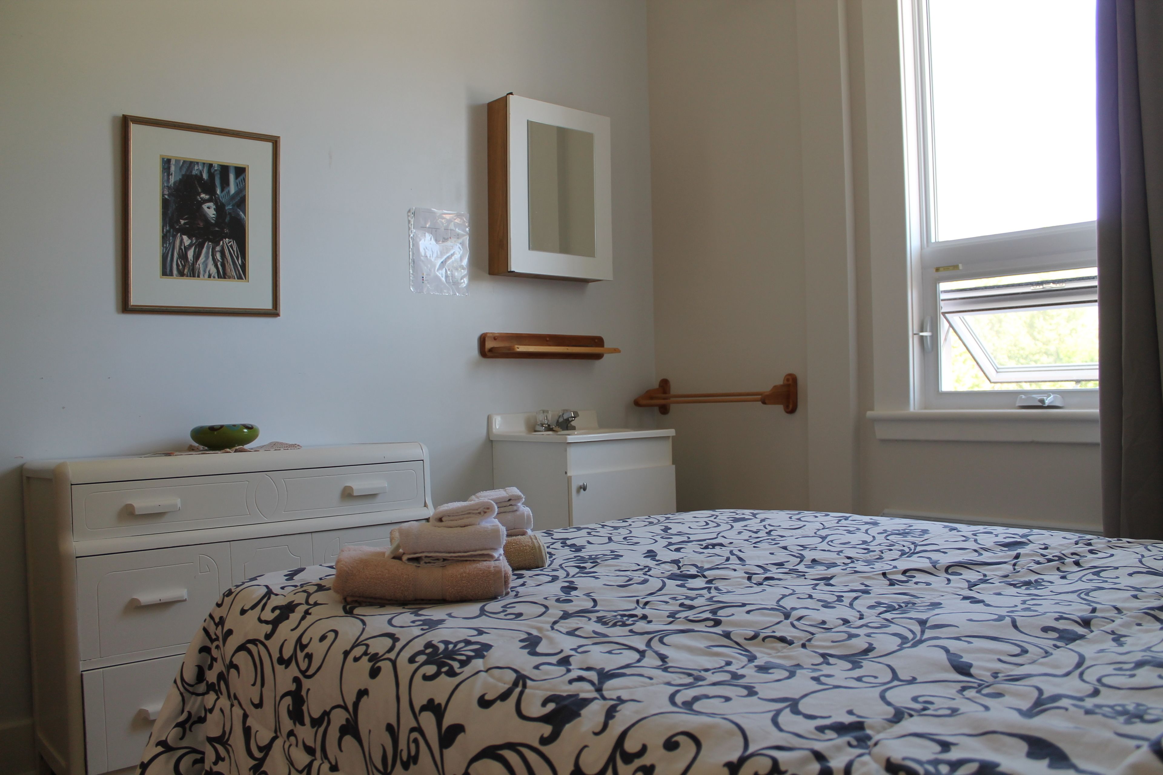 Un dormitorio con cama, cómoda, espejo y ventana.