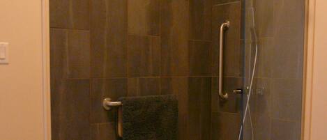 A glass-enclosed shower with a black floor, a towel rack, and a handrail.