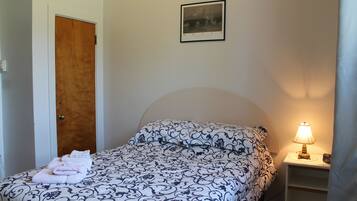 A bedroom with a bed, a nightstand with a lamp, a door, and a framed picture on the wall.
