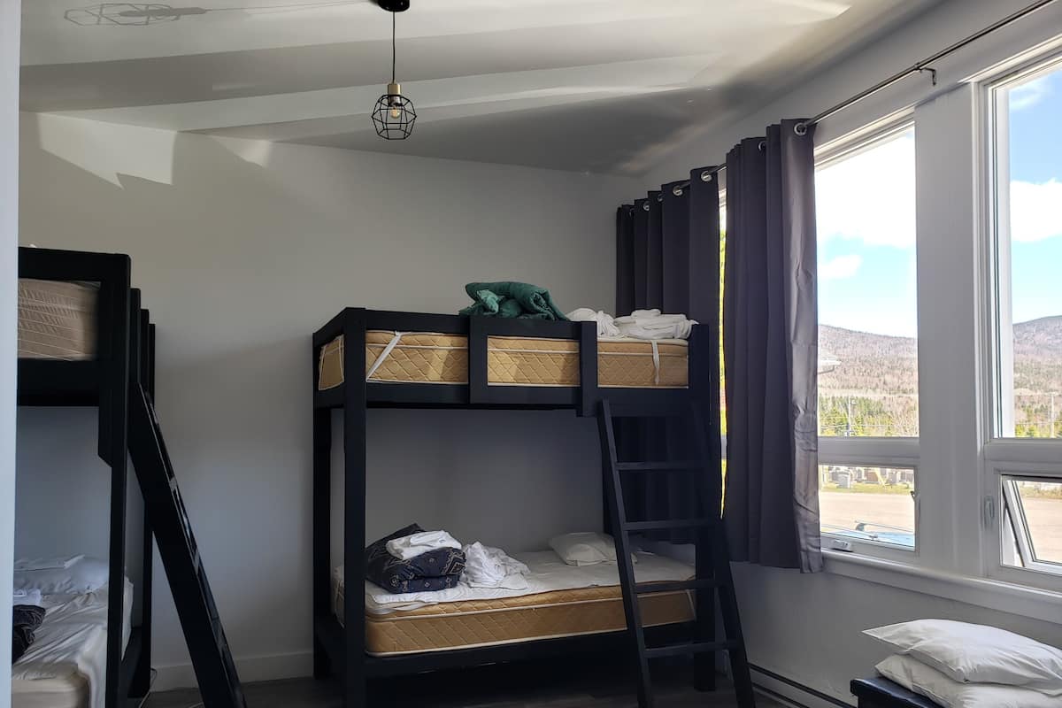 Habitación con literas, una escalera, una ventana con cortinas y una lámpara colgante.