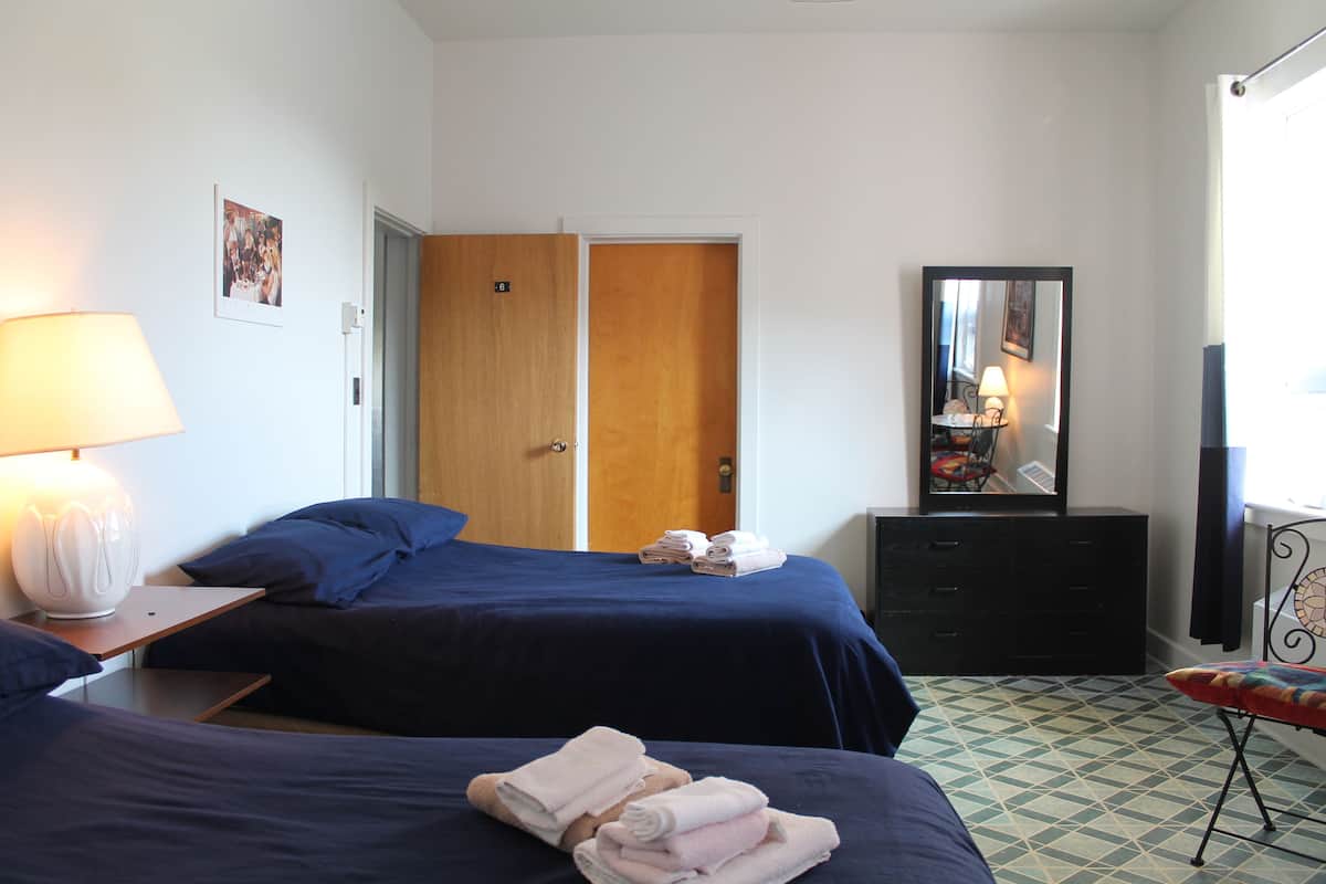Habitación de hotel con dos camas, una puerta de madera, un aparador, un espejo y una lámpara.