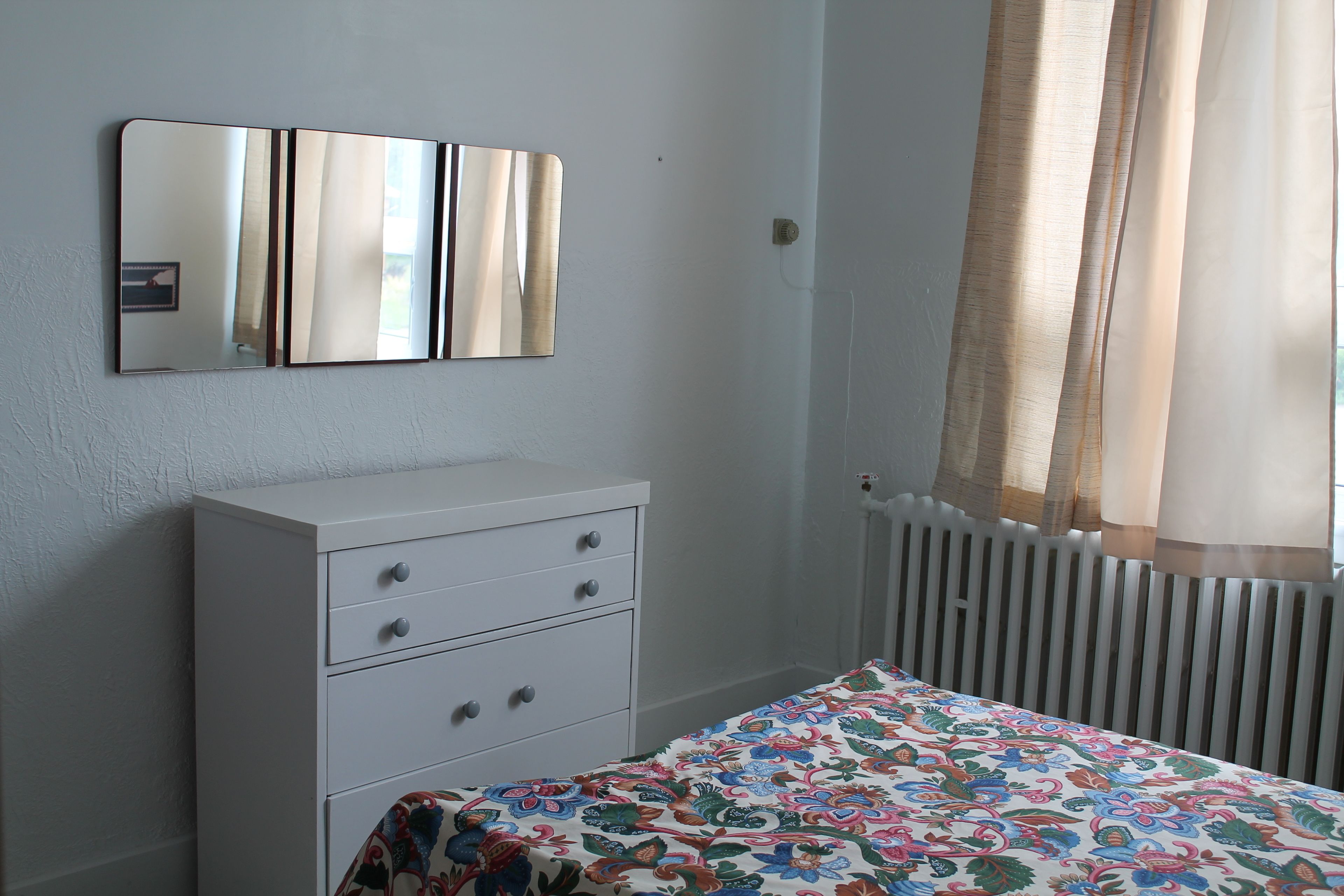 A bedroom with a bed, a dresser, a mirror, and a window with curtains.