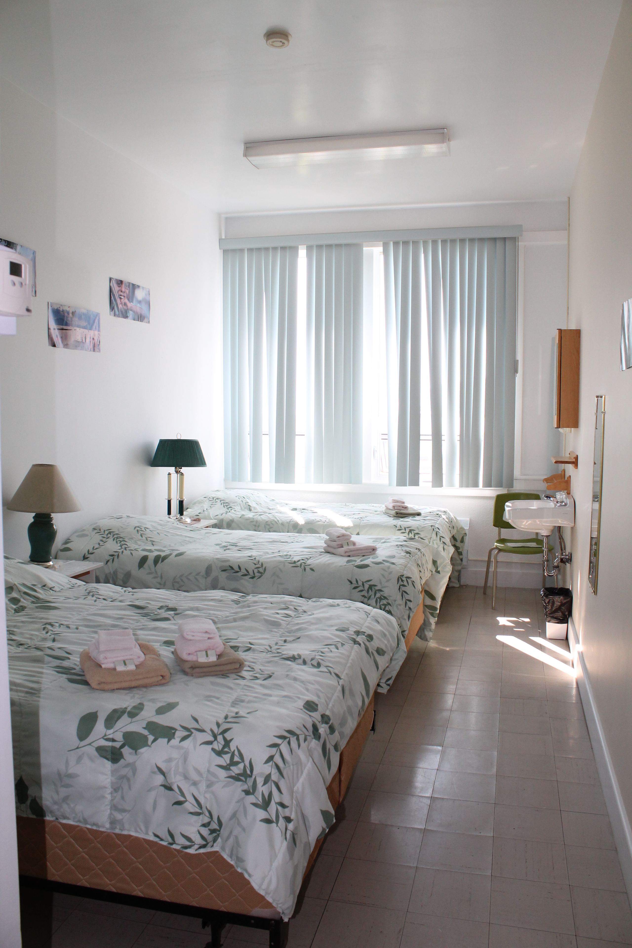 Habitación de hotel con dos camas, una silla verde, un lavabo y un espejo.