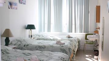 Habitación de hotel con dos camas, una silla verde, un lavabo y un espejo.