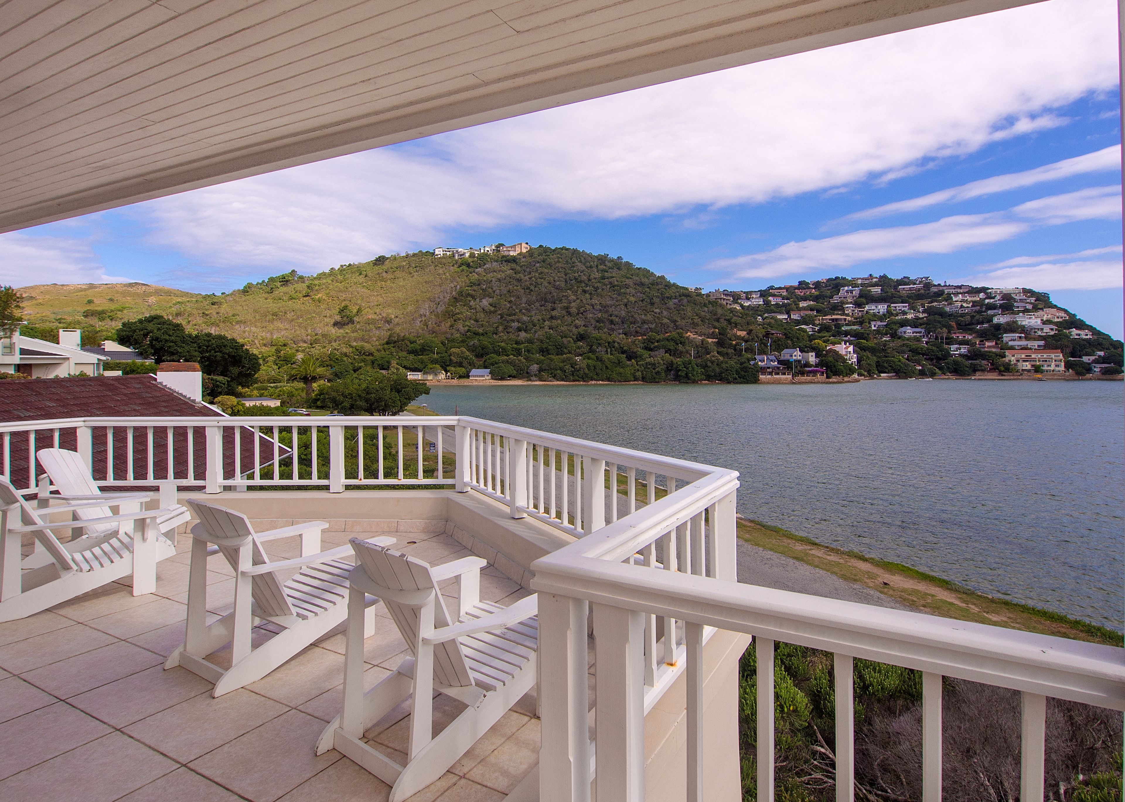A balcony with white railings overlooking a lake, surrounded by greenery and houses.