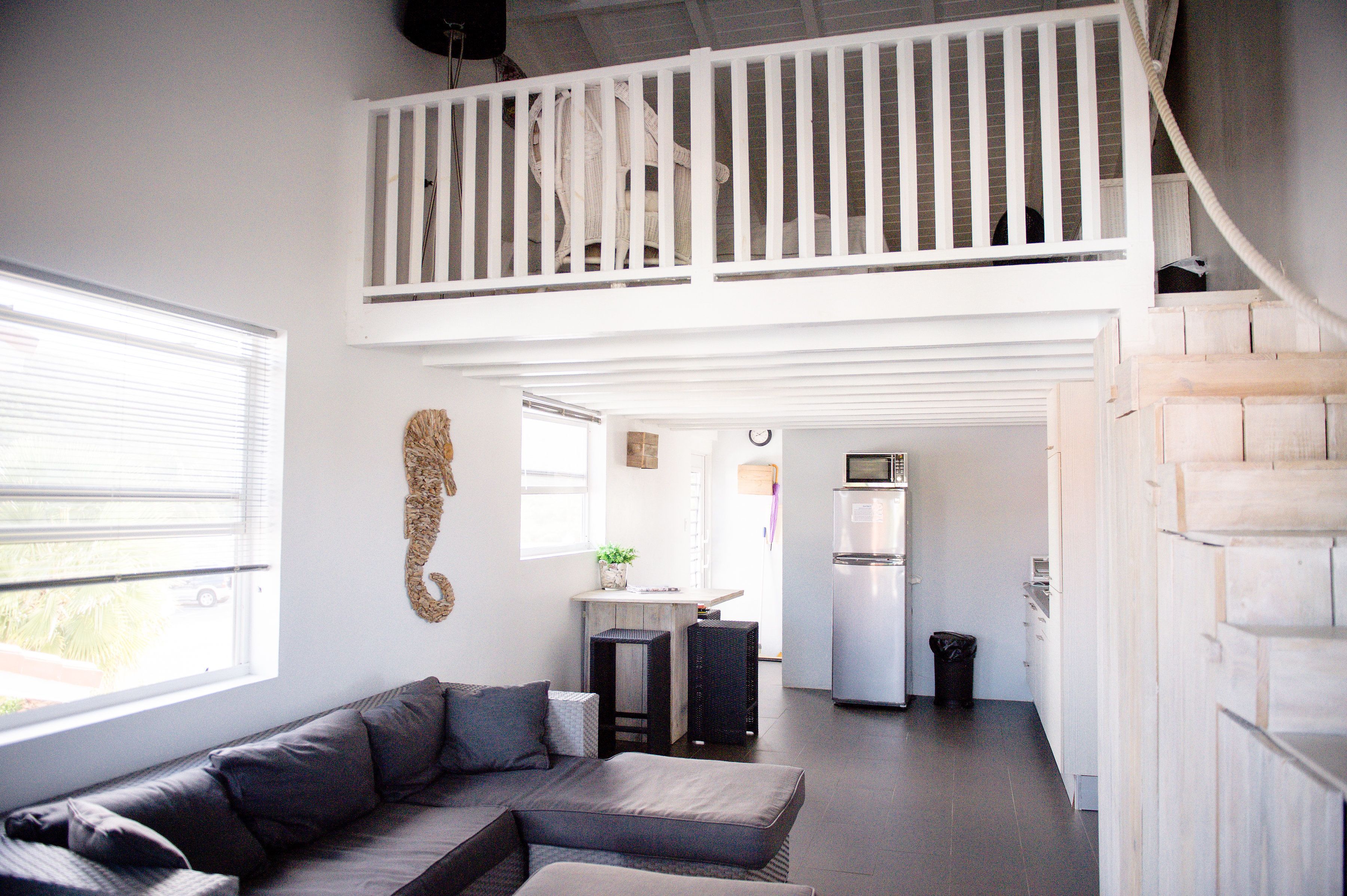 A spacious living area with a high ceiling, a built-in kitchen, and a balcony.