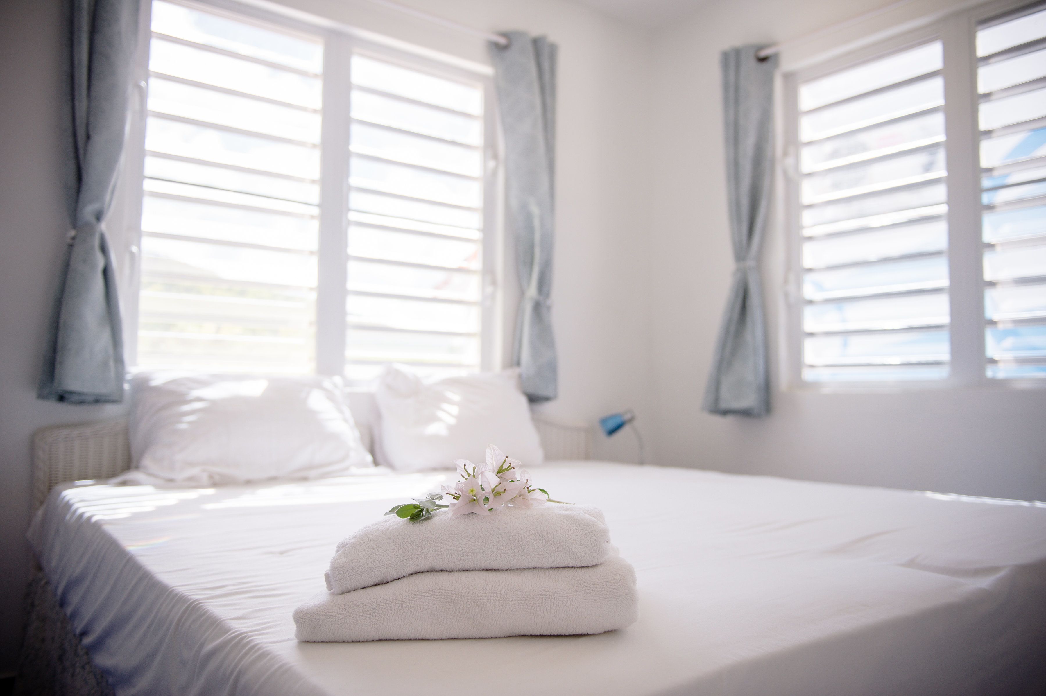 A neatly made bed with white linens and a stack of white towels.