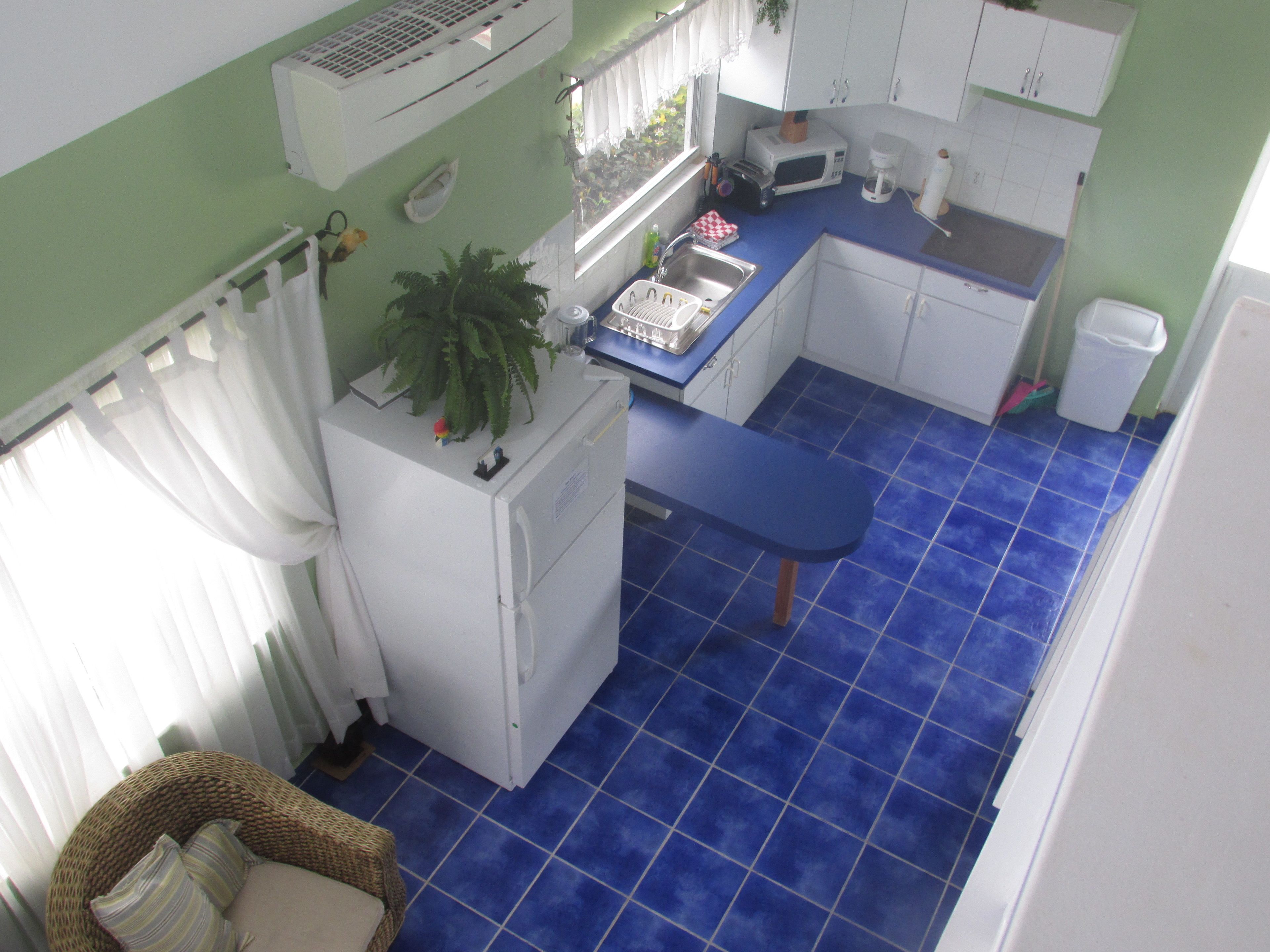 A compact kitchen with a blue tiled floor, white cabinets, and a small dining area with a bench.