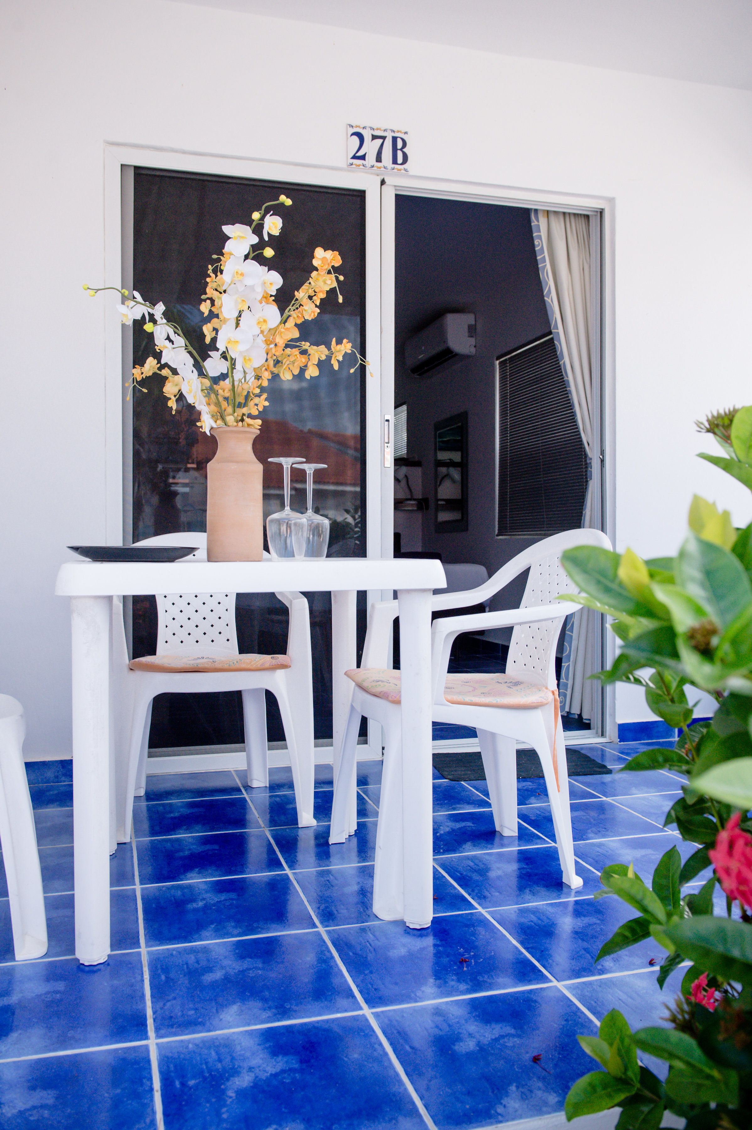 A white table with two chairs, a vase with flowers, and a number sign above the door.