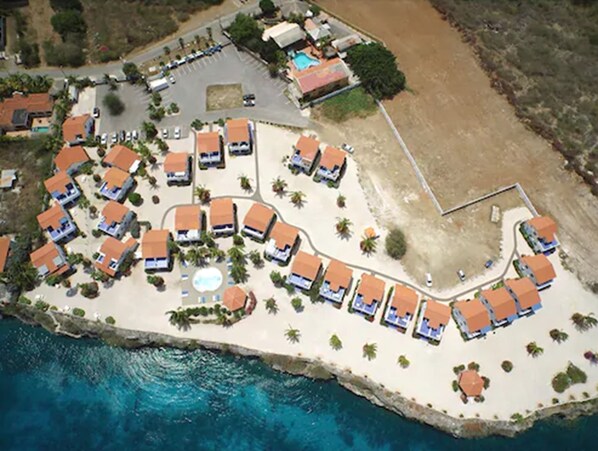 Vue aérienne d’une station balnéaire comprenant plusieurs hébergements de type bungalow, une piscine centrale et une plage de sable.