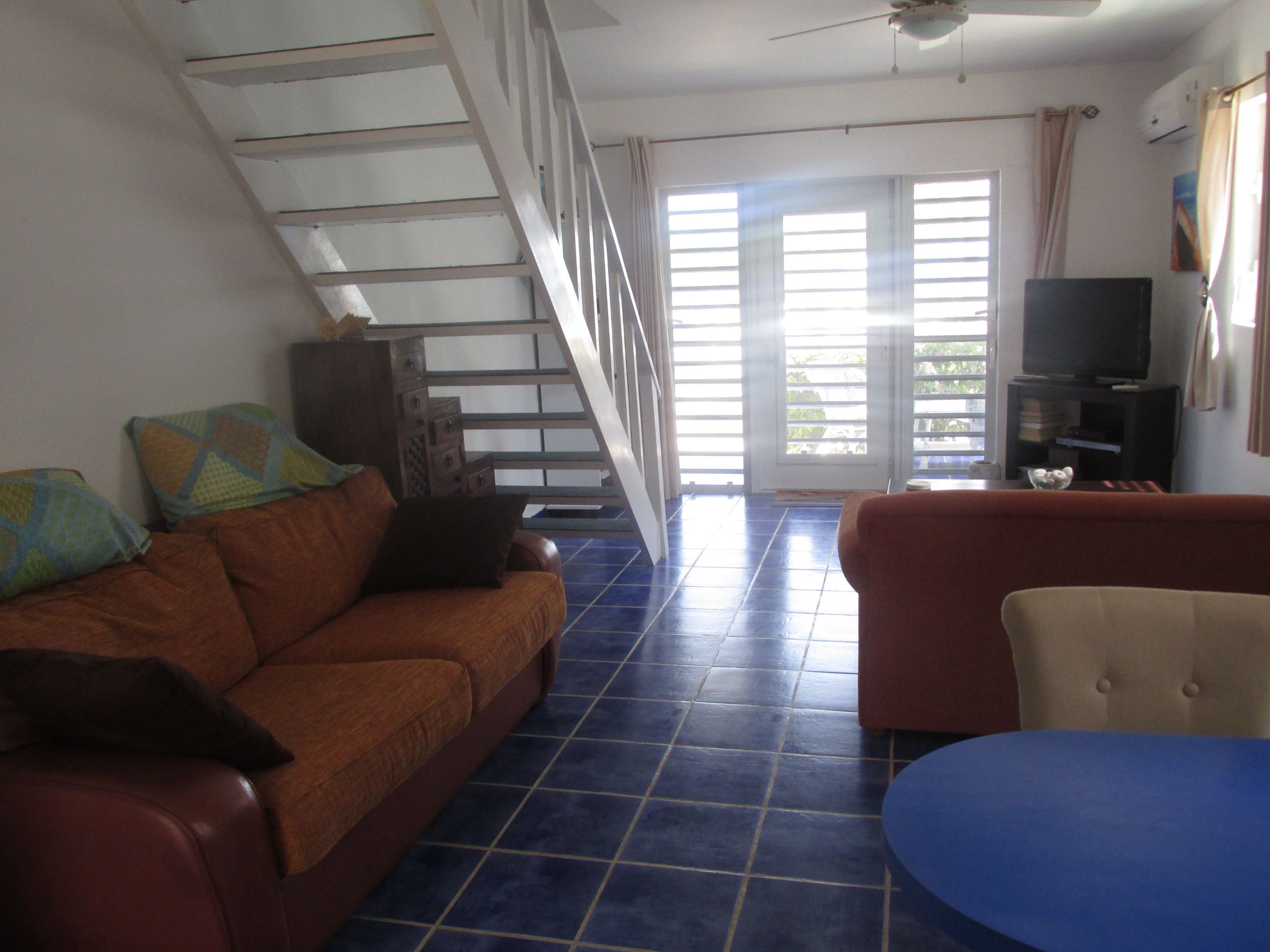 A living room with a brown sofa, a blue ottoman, a television, and a staircase.