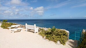 Een strand met witte banken en tafels, een rotsachtige rand en uitzicht op de oceaan.