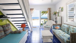Een lichte woonkamer met een bank, fauteuil, poef, een trap en uitzicht op de oceaan.